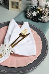 Photo of Christmas table setting with plates, cutlery and festive decor on light grey background, closeup