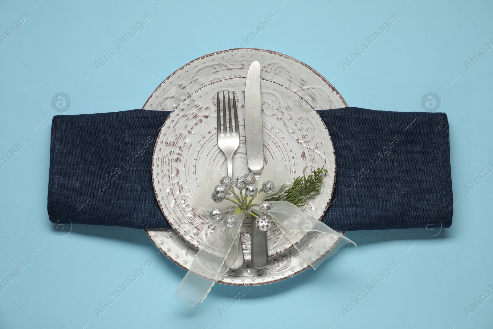 Photo of Christmas table setting with plates, cutlery and festive decor on light blue background, top view