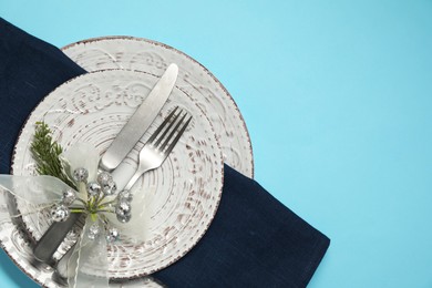 Photo of Christmas table setting with plates, cutlery and festive decor on light blue background, top view. Space for text