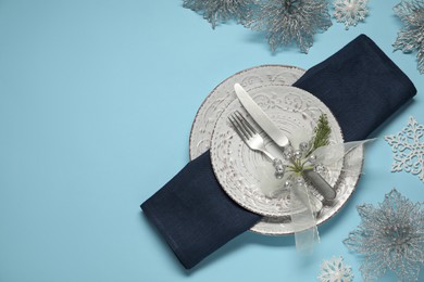 Photo of Christmas table setting with plates, cutlery and festive decor on light blue background, top view. Space for text