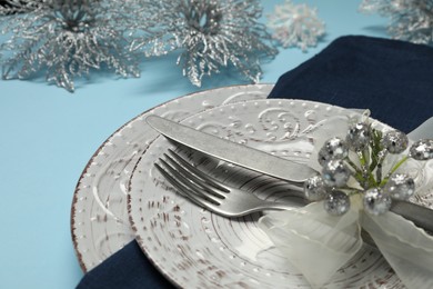 Photo of Christmas table setting with plates, cutlery and festive decor on light blue background, closeup