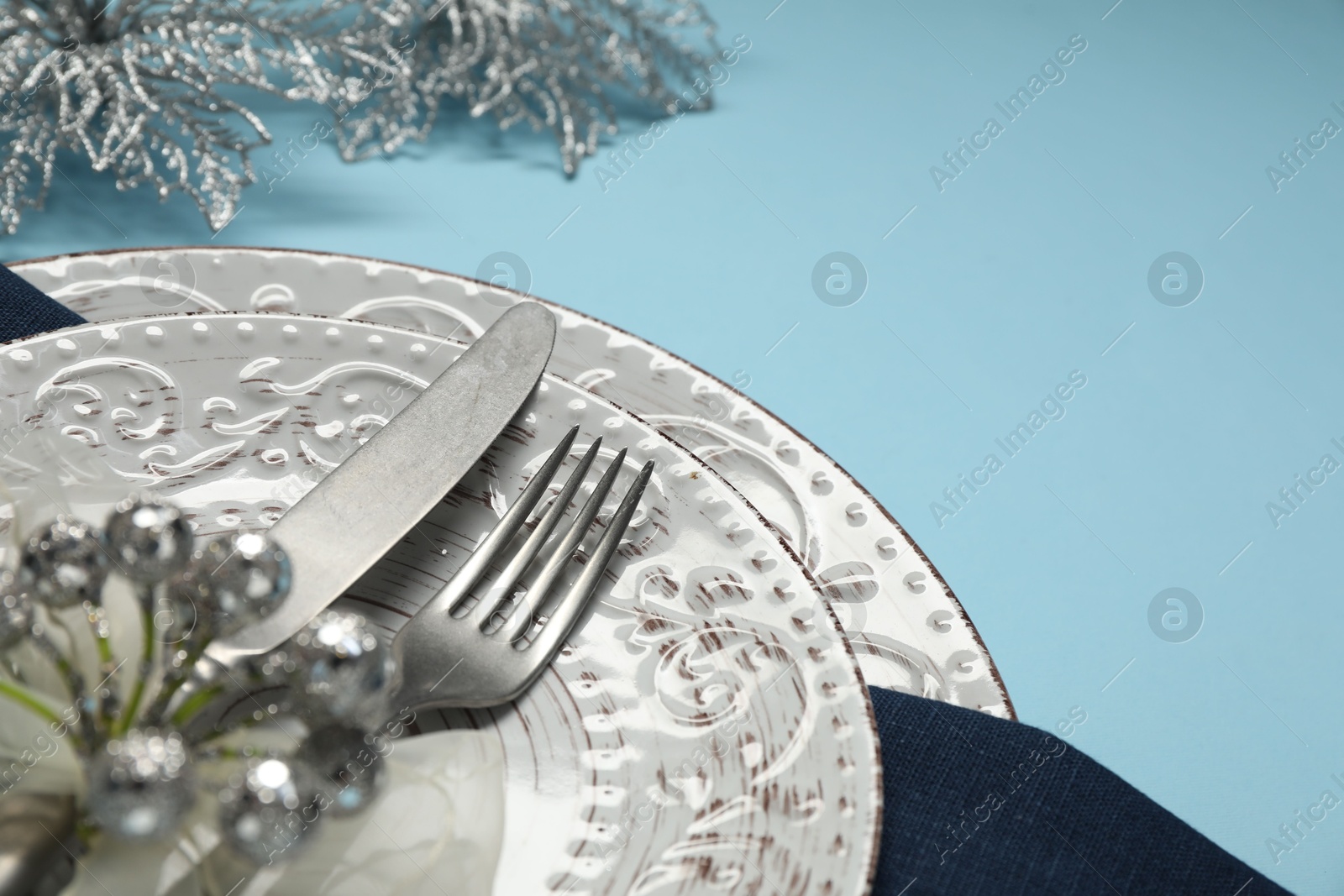 Photo of Christmas table setting with plates, cutlery and festive decor on light blue background, closeup