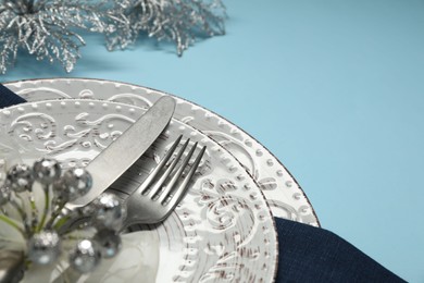 Photo of Christmas table setting with plates, cutlery and festive decor on light blue background, closeup