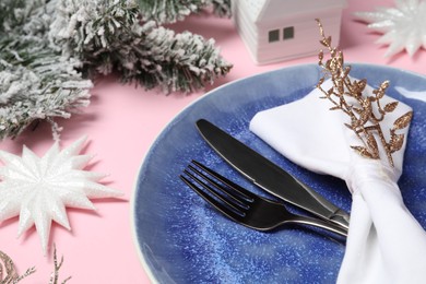 Photo of Christmas table setting with plate, cutlery and festive decor on pink background, closeup