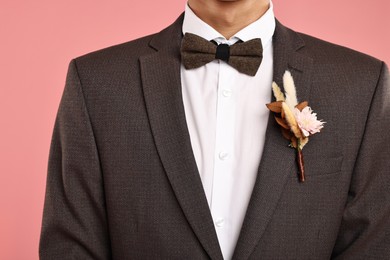 Photo of Groom in suit with stylish boutonniere on pink background, closeup