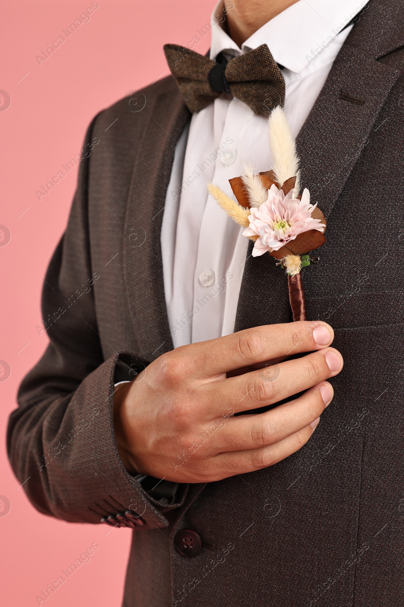 Photo of Groom in suit with stylish boutonniere on pink background, closeup