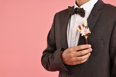 Photo of Groom in suit with stylish boutonniere on pink background, closeup. Space for text