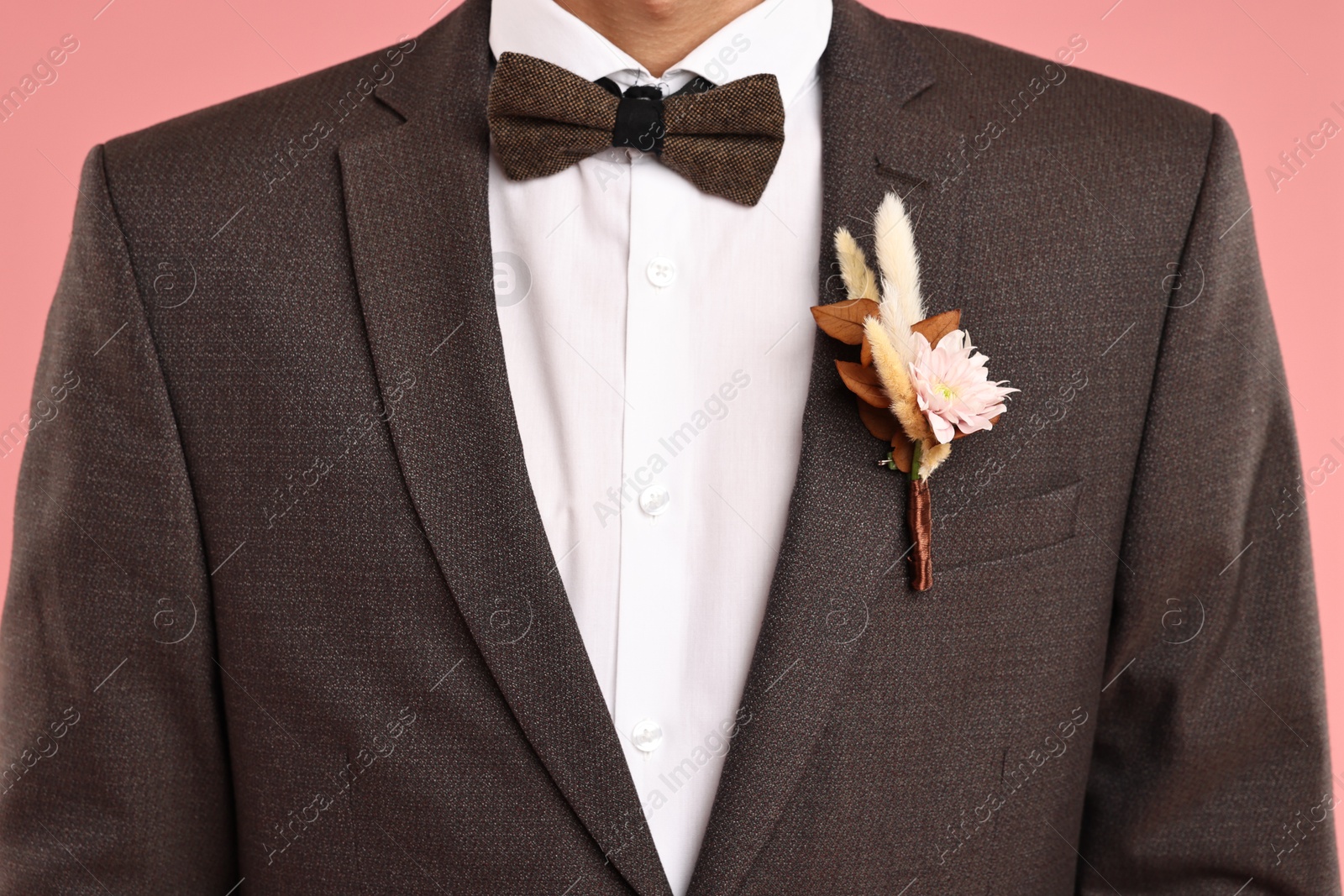 Photo of Groom in suit with stylish boutonniere on pink background, closeup