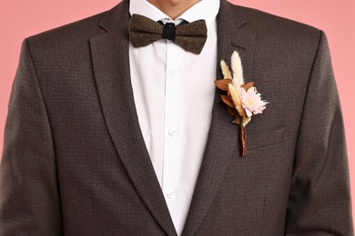 Photo of Groom in suit with stylish boutonniere on pink background, closeup