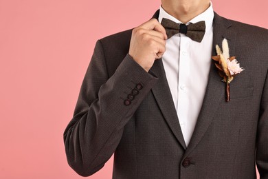 Photo of Groom in suit with stylish boutonniere on pink background, closeup