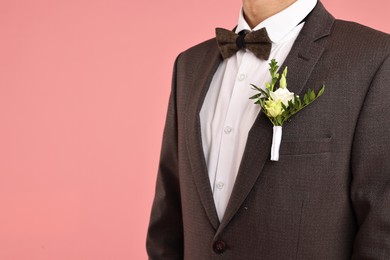 Photo of Groom in suit with stylish boutonniere on pink background, closeup. Space for text