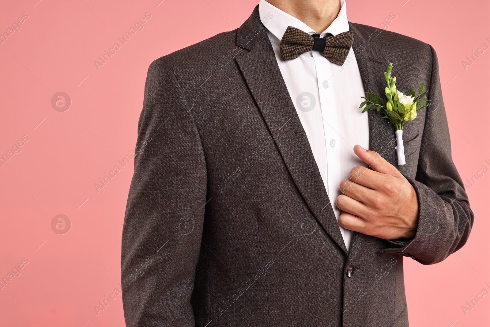 Photo of Groom in suit with stylish boutonniere on pink background, closeup