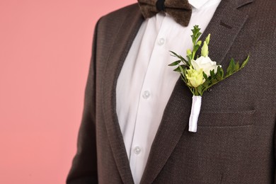 Photo of Groom in suit with stylish boutonniere on pink background, closeup. Space for text