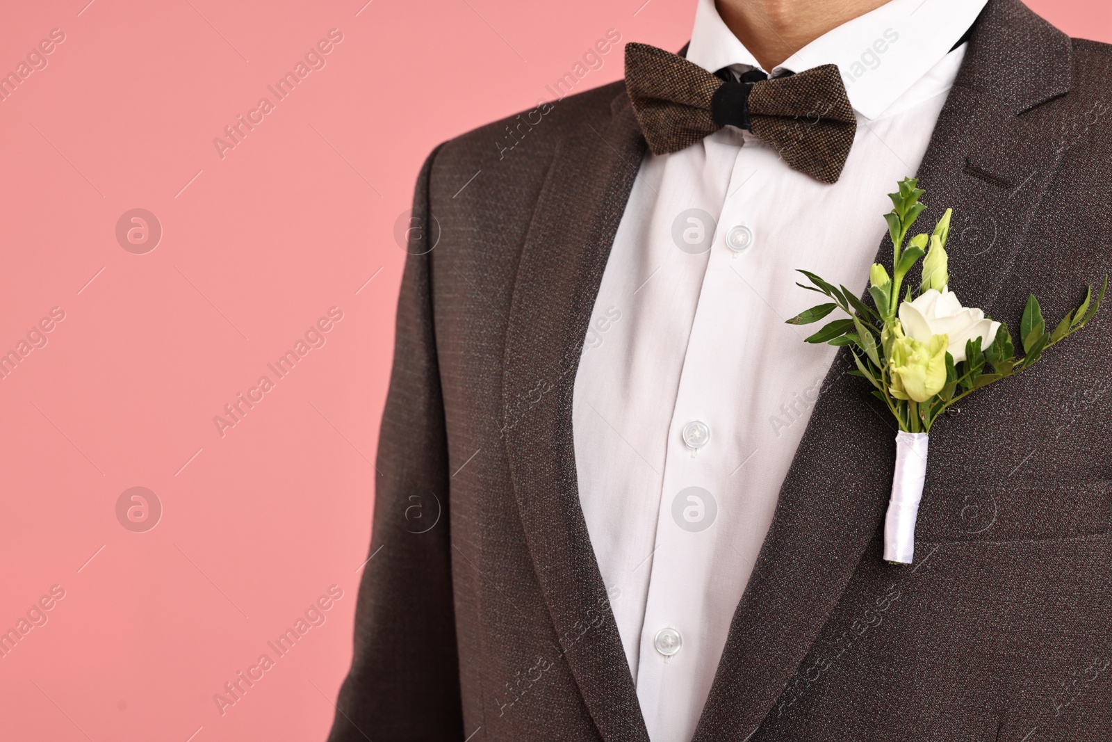 Photo of Groom in suit with stylish boutonniere on pink background, closeup. Space for text