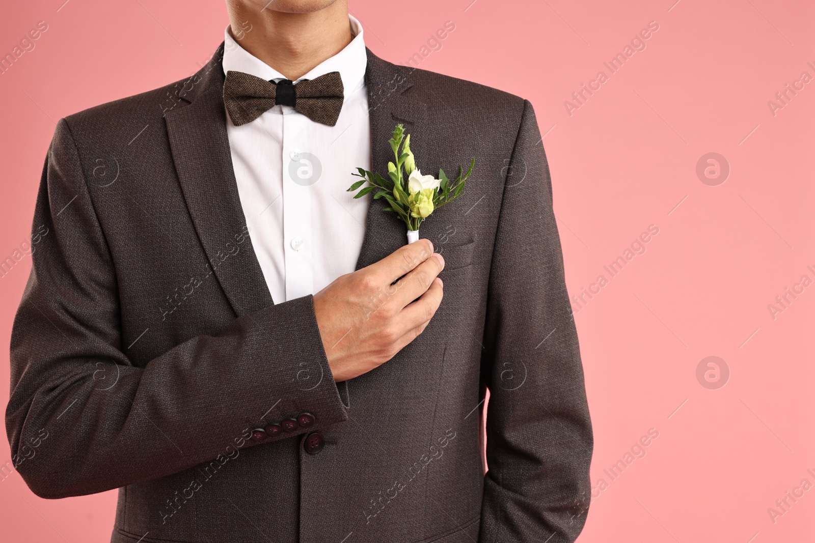 Photo of Groom in suit with stylish boutonniere on pink background, closeup. Space for text