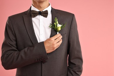 Photo of Groom in suit with stylish boutonniere on pink background, closeup. Space for text