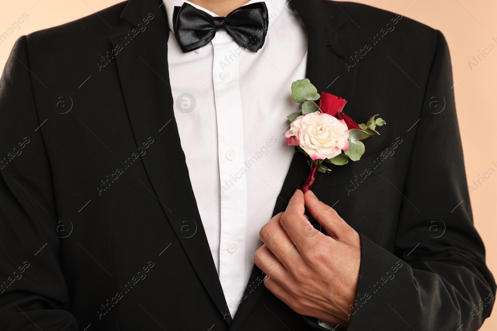 Photo of Groom in suit with stylish boutonniere on beige background, closeup