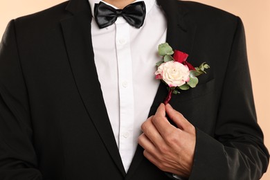 Photo of Groom in suit with stylish boutonniere on beige background, closeup