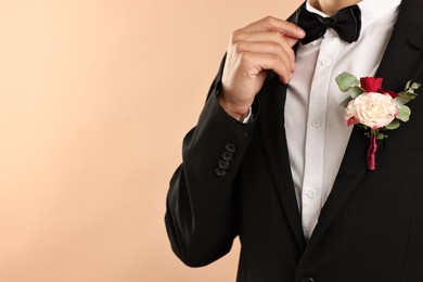 Photo of Groom in suit with stylish boutonniere on beige background, closeup. Space for text