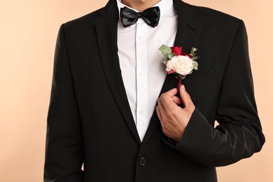 Photo of Groom in suit with stylish boutonniere on beige background, closeup