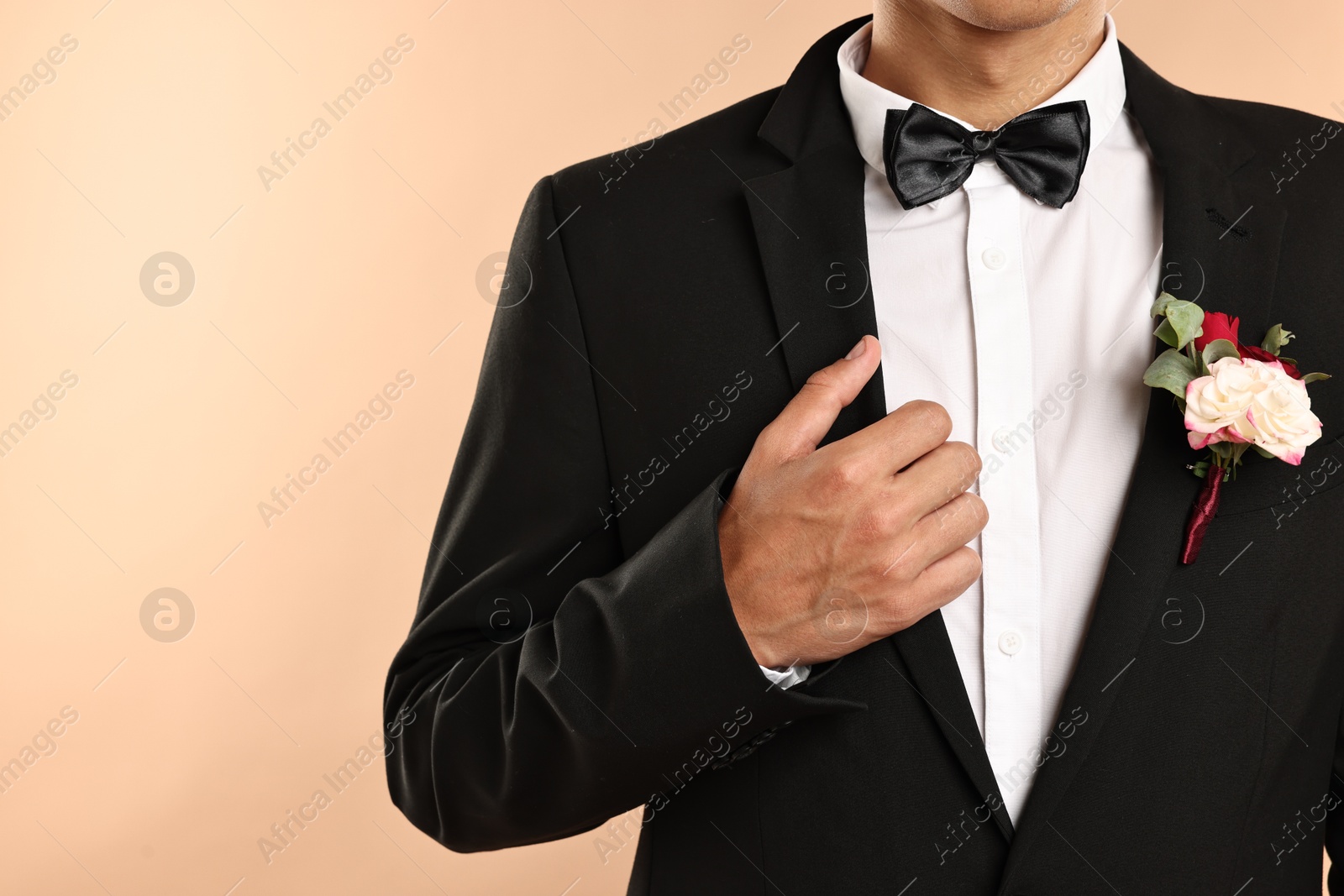 Photo of Groom in suit with stylish boutonniere on beige background, closeup. Space for text