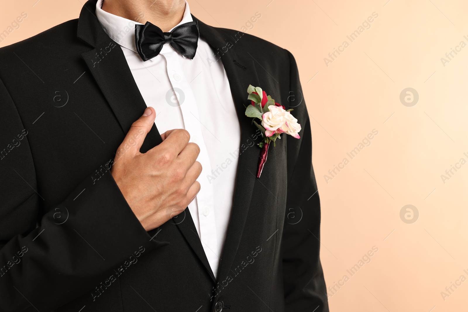 Photo of Groom in suit with stylish boutonniere on beige background, closeup. Space for text