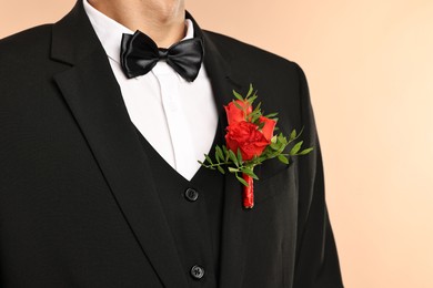 Photo of Groom in suit with stylish boutonniere on beige background, closeup