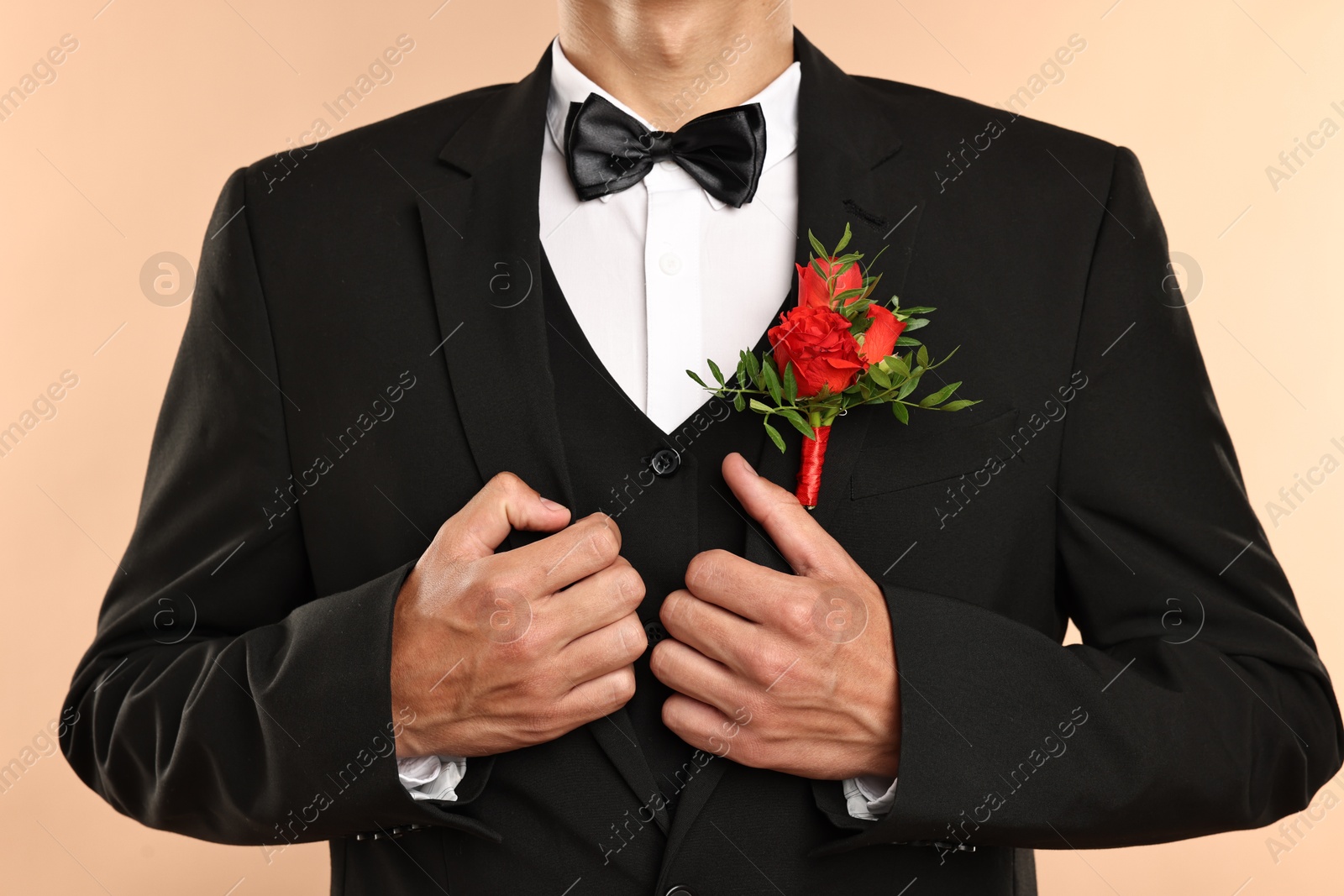 Photo of Groom in suit with stylish boutonniere on beige background, closeup