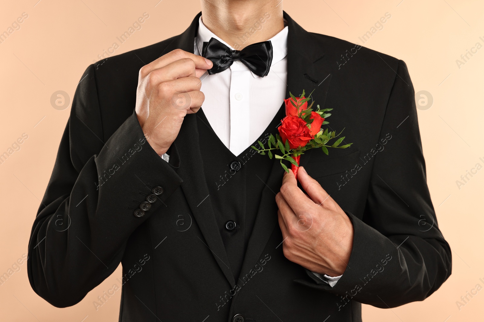 Photo of Groom in suit with stylish boutonniere on beige background, closeup