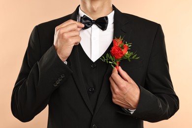 Photo of Groom in suit with stylish boutonniere on beige background, closeup