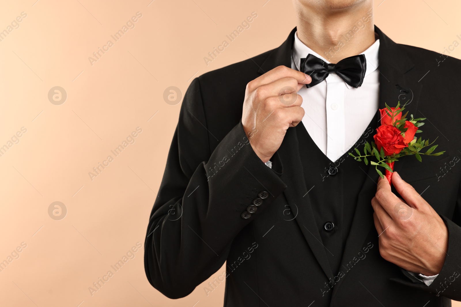 Photo of Groom in suit with stylish boutonniere on beige background, closeup. Space for text