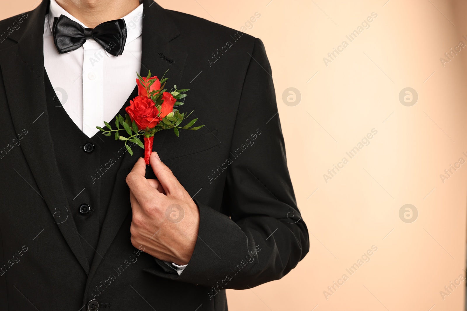 Photo of Groom in suit with stylish boutonniere on beige background, closeup. Space for text