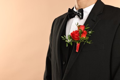 Photo of Groom in suit with stylish boutonniere on beige background, closeup. Space for text