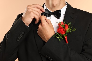 Photo of Groom in suit with stylish boutonniere on beige background, closeup