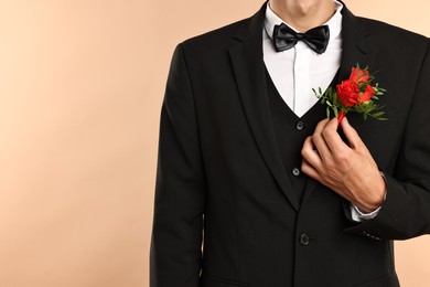 Photo of Groom in suit with stylish boutonniere on beige background, closeup. Space for text