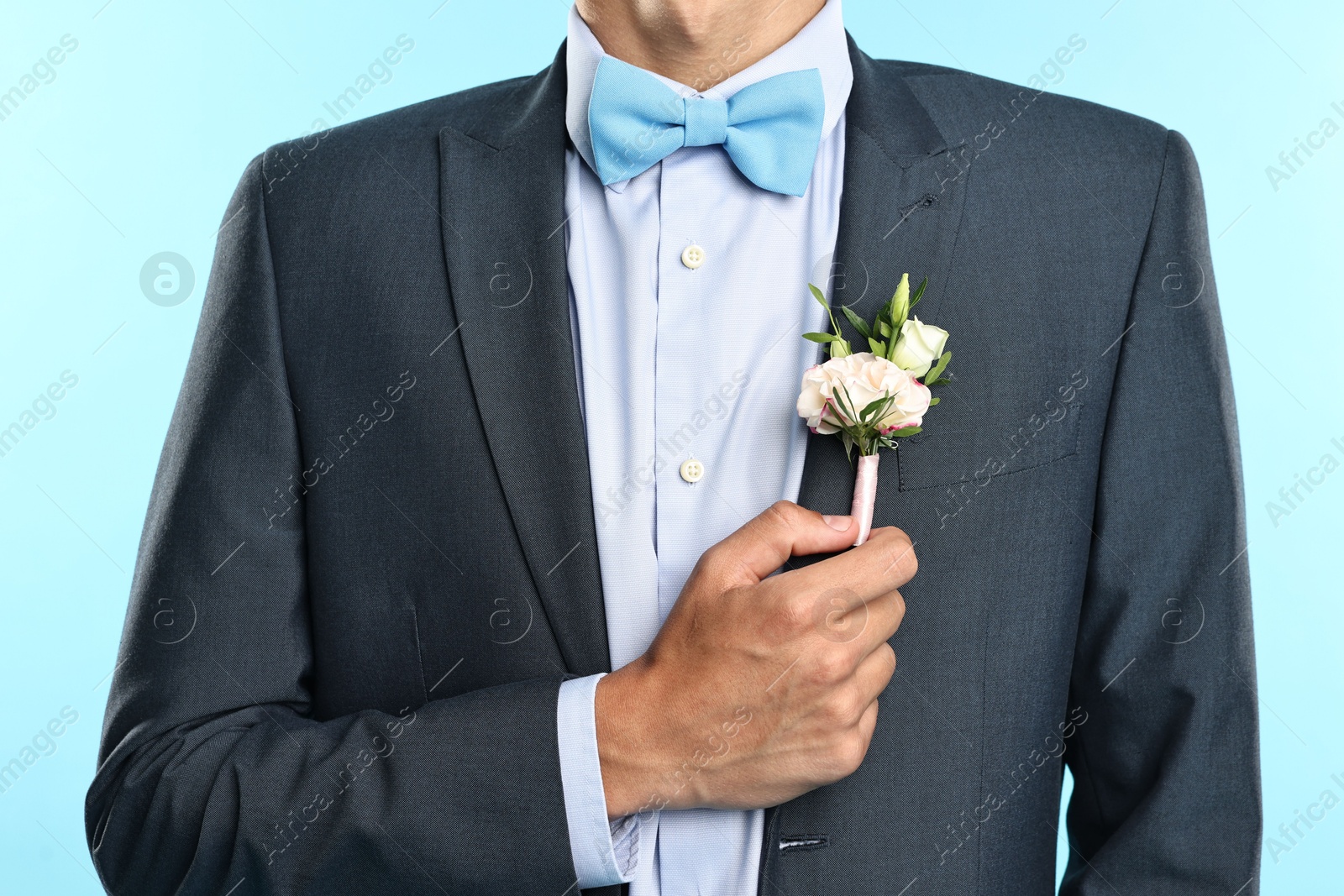 Photo of Groom in suit with stylish boutonniere on light blue background, closeup