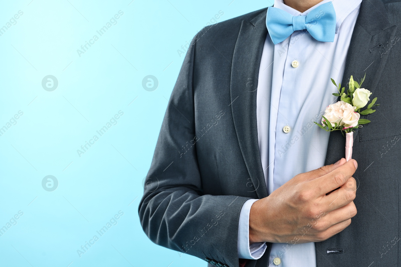 Photo of Groom in suit with stylish boutonniere on light blue background, closeup. Space for text