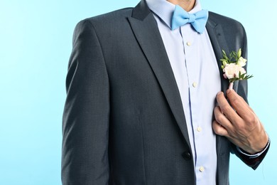 Photo of Groom in suit with stylish boutonniere on light blue background, closeup