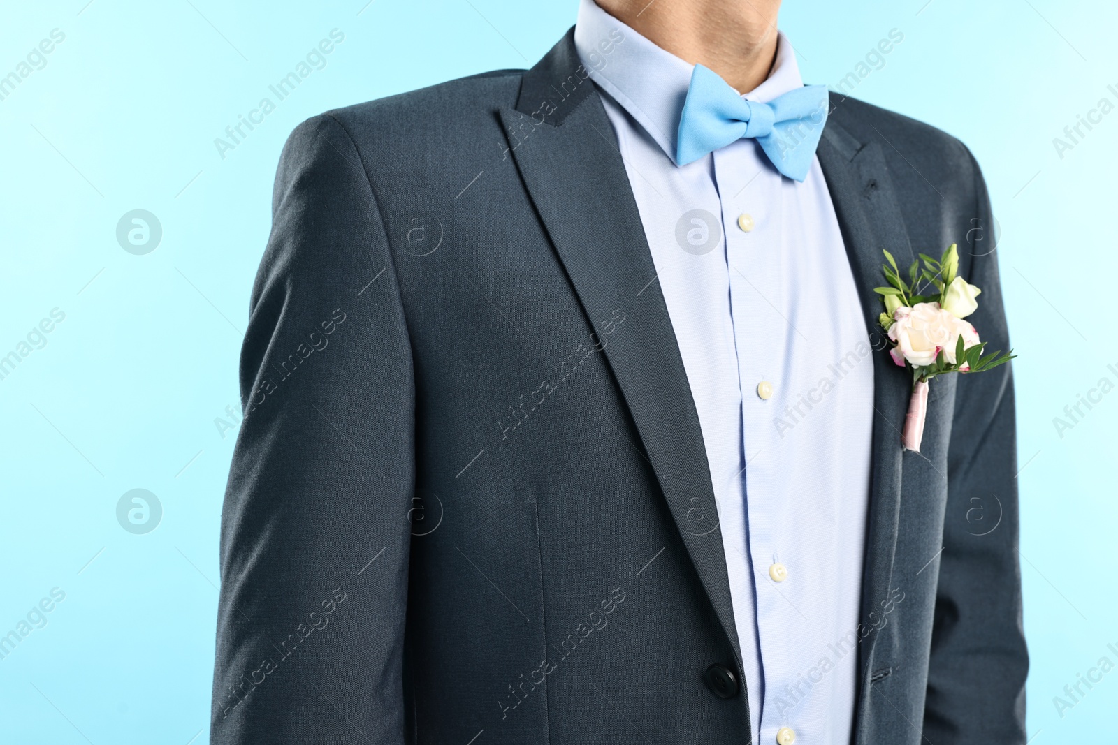 Photo of Groom in suit with stylish boutonniere on light blue background, closeup