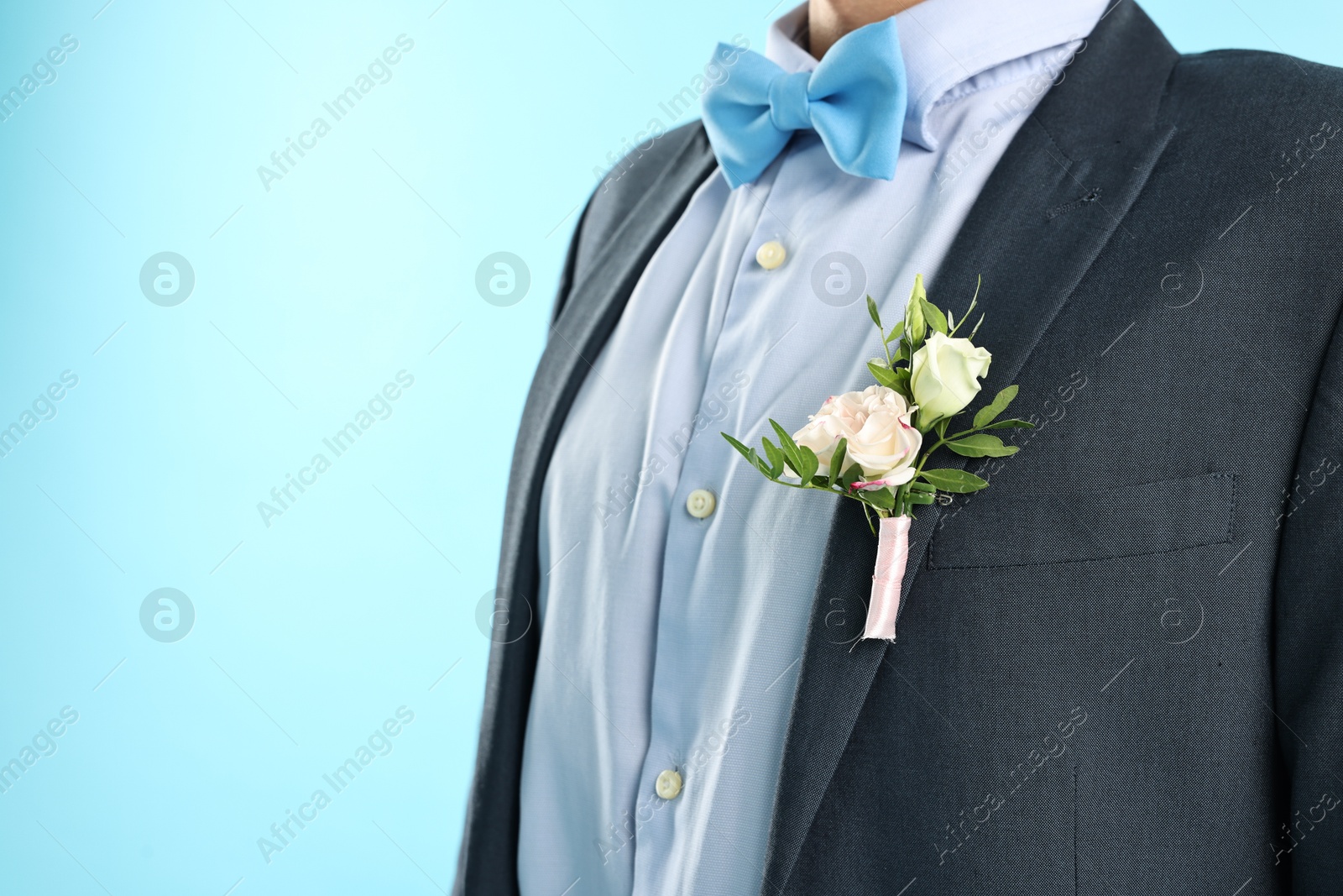 Photo of Groom in suit with stylish boutonniere on light blue background, closeup. Space for text