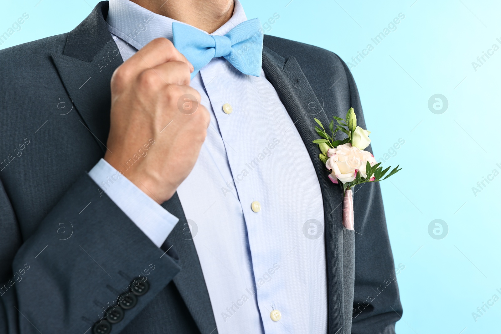 Photo of Groom in suit with stylish boutonniere on light blue background, closeup