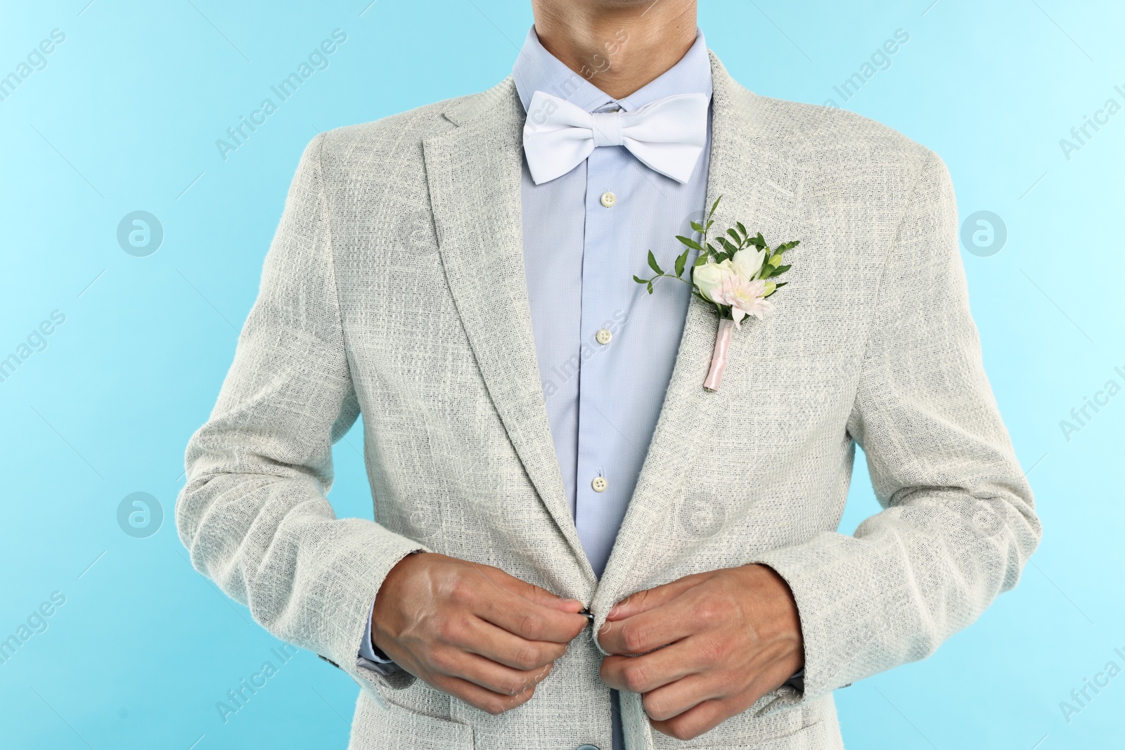 Photo of Groom in suit with stylish boutonniere on light blue background, closeup