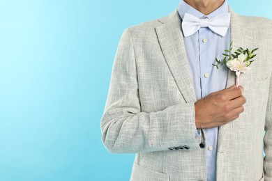 Photo of Groom in suit with stylish boutonniere on light blue background, closeup. Space for text