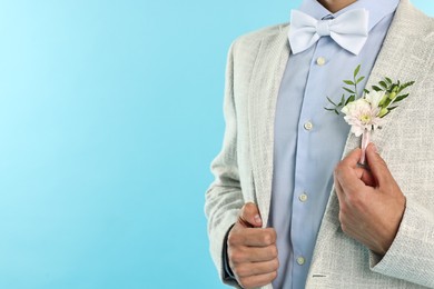 Photo of Groom in suit with stylish boutonniere on light blue background, closeup. Space for text