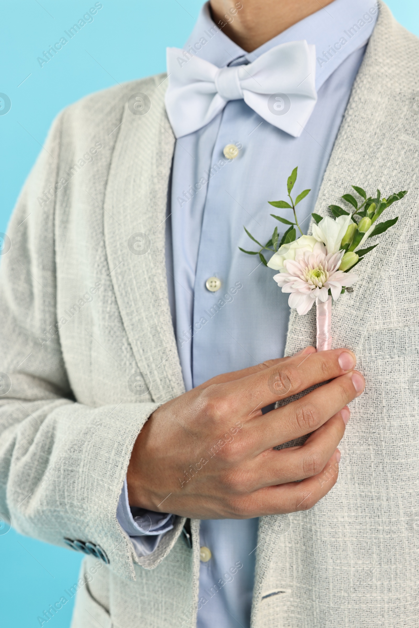 Photo of Groom in suit with stylish boutonniere on light blue background, closeup