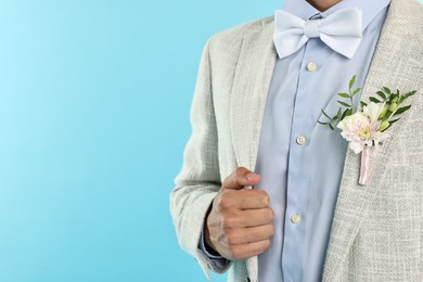 Photo of Groom in suit with stylish boutonniere on light blue background, closeup. Space for text