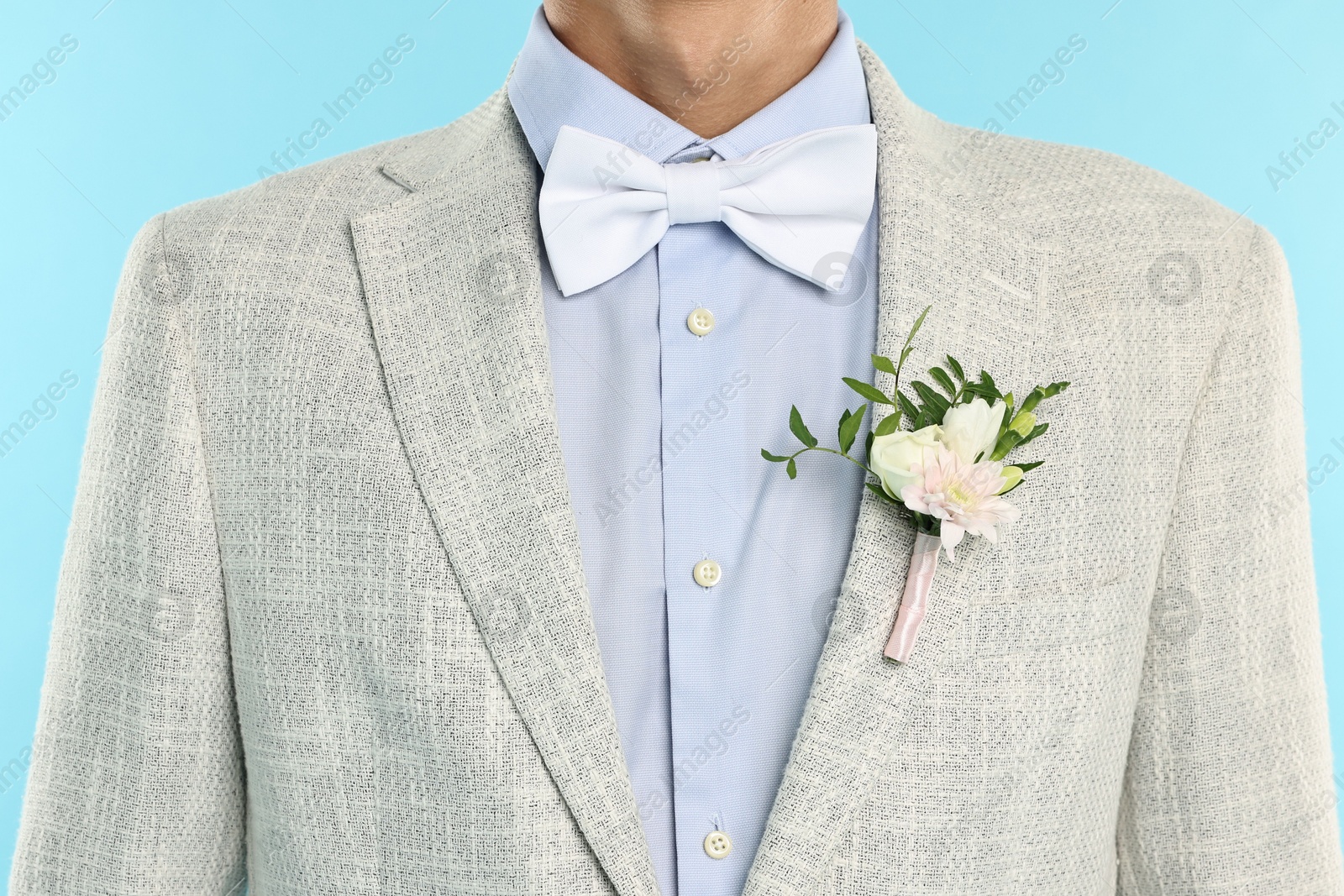 Photo of Groom in suit with stylish boutonniere on light blue background, closeup