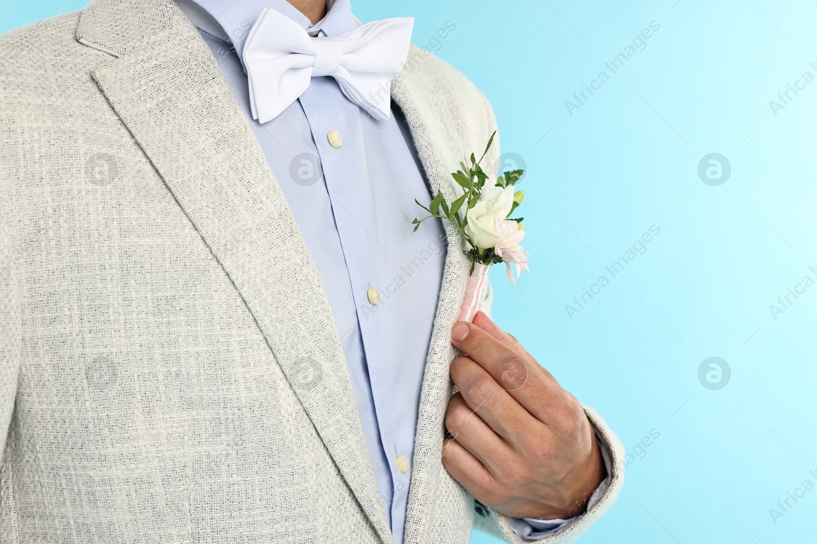 Photo of Groom in suit with stylish boutonniere on light blue background, closeup. Space for text