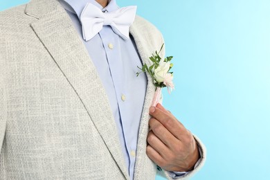 Photo of Groom in suit with stylish boutonniere on light blue background, closeup. Space for text