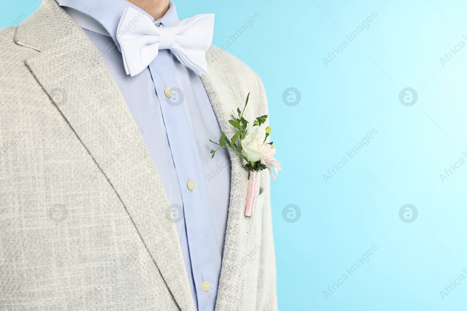 Photo of Groom in suit with stylish boutonniere on light blue background, closeup. Space for text